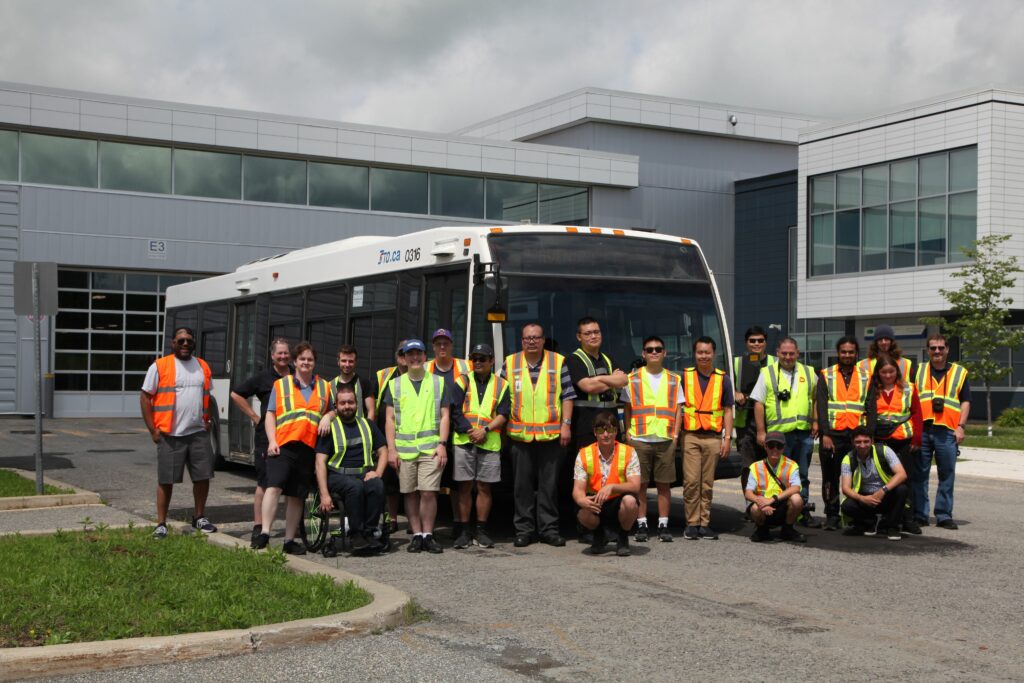 Charter participants wearing safety vests pose in front of a white STO bus, parked outside the modern Gatineau Garage